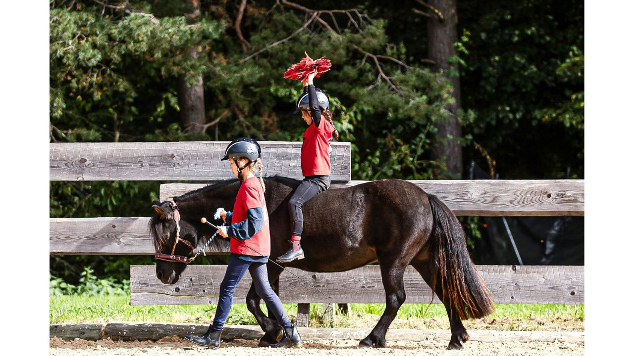 Kind führt Pony mit Reiterkind, das mit einer Wollebommel die Balance übt, im HIPPOLINI Kurs 1
